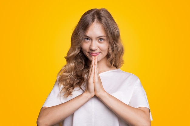 Junges europäisches mädchen auf gelbem hintergrund mit blonden und welligen haaren porträt einer frau, die lächelt und ho...