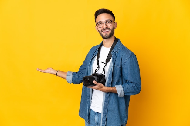 Junges Fotografmädchen lokalisiert auf gelbem Hintergrund, der Hände zur Seite für die Einladung zum Kommen ausdehnt