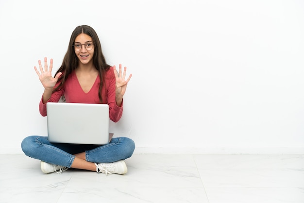 Junges französisches Mädchen, das auf dem Boden mit ihrem Laptop sitzt, der neun mit den Fingern zählt