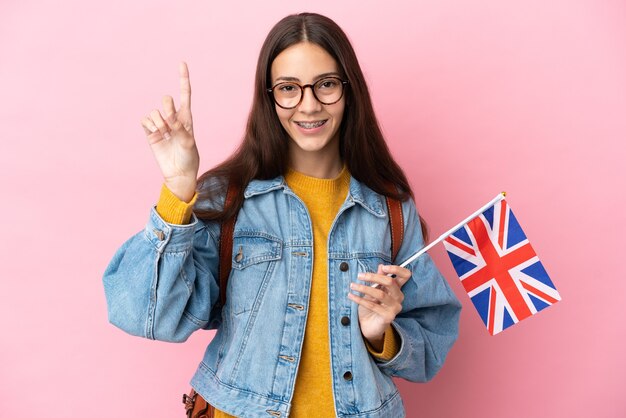 Junges französisches Mädchen, das eine britische Flagge lokalisiert auf rosa Wand hält, die eine große Idee aufzeigt