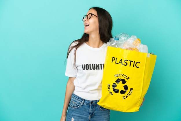 Junges französisches Mädchen, das eine Tasche voller Plastikflaschen hält, um lachend in Seitenlage zu recyceln