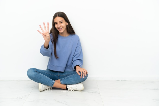 Junges französisches Mädchen, das glücklich auf dem Boden sitzt und vier mit den Fingern zählt