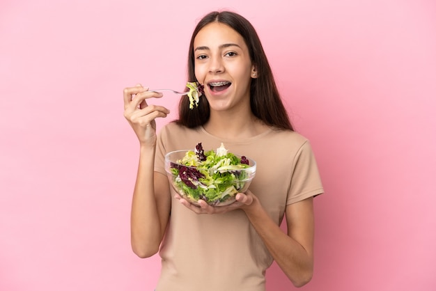 Junges französisches Mädchen isoliert auf rosa Hintergrund, das eine Schüssel Salat mit glücklichem Ausdruck hält