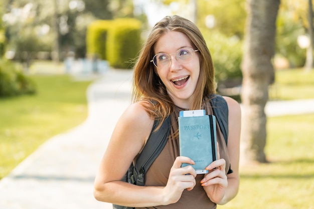 Foto junges französisches mädchen mit brille im freien hält ein pass mit überraschtem ausdruck