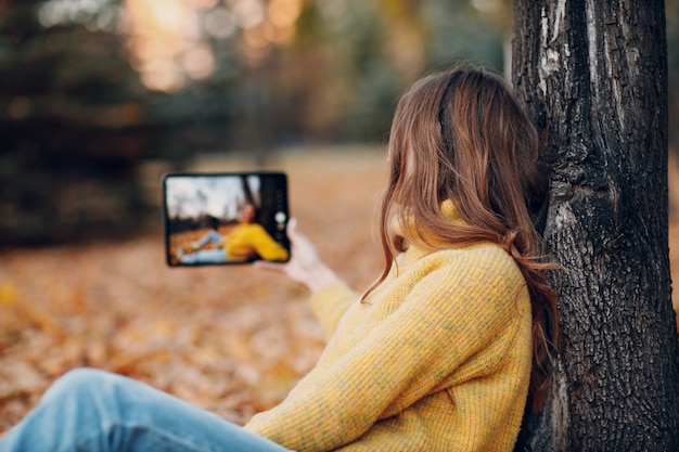 Junges Frauenmodell macht Selfie-Foto mit Tablet-PC im Herbstpark mit gelben Laub-Ahornblättern. Mode für die Herbstsaison