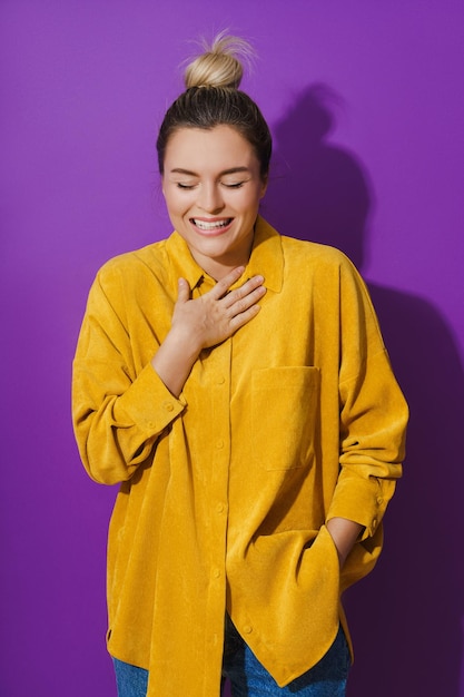 Junges fröhliches lachendes Mädchen mit gelbem Hemd vor violettem Hintergrund