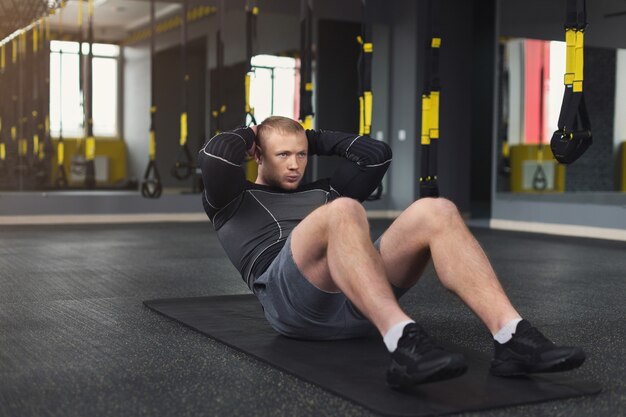 Junges, fröhliches Manntraining im Fitnessclub. Porträt eines Kaukasiers, der Übungen, Sit-ups und Crunches für Bauchmuskeln macht, drinnen im Fitnessstudio trainiert, Platz kopiert