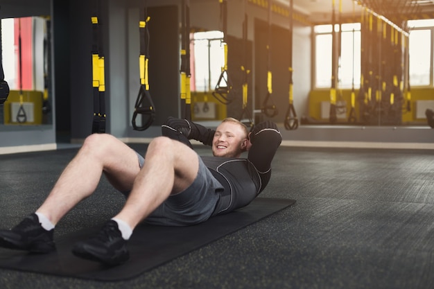 Junges, fröhliches Manntraining im Fitnessclub. Porträt eines Kaukasiers, der Übungen, Sit-ups und Crunches für Bauchmuskeln macht, drinnen im Fitnessstudio trainiert, Platz kopiert