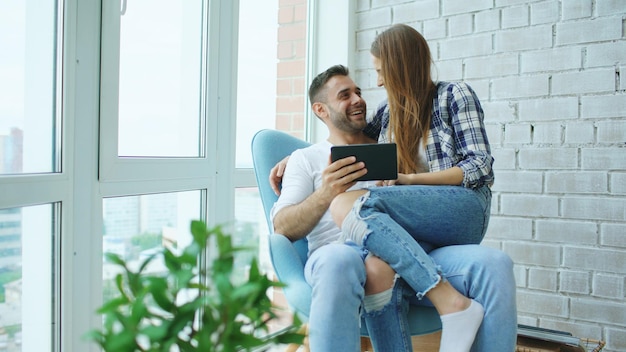 Junges fröhliches Paar spricht und benutzt Tablet-Computer auf Balkon in moderner Loft-Wohnung