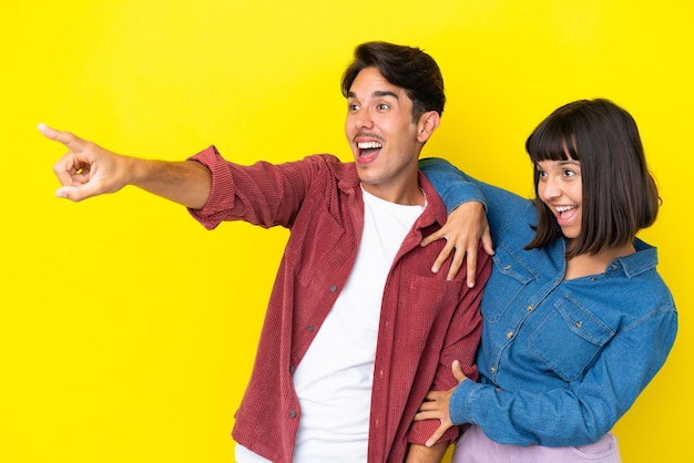 Junges gemischtes Paar auf gelbem Hintergrund, das eine Idee präsentiert, während sie lächelnd in Richtung blickt