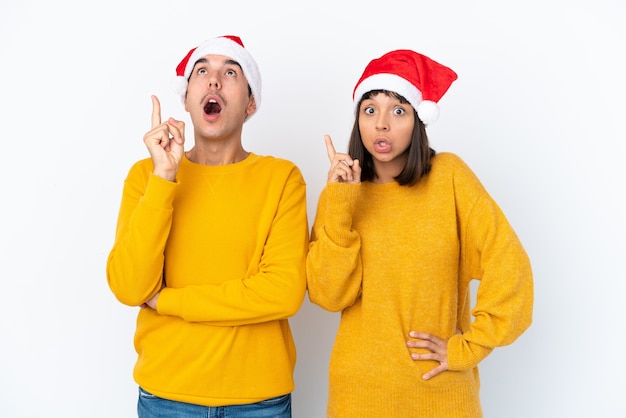 Junges gemischtes Paar feiert Weihnachten isoliert auf weißem Hintergrund und denkt eine Idee, die mit dem Finger nach oben zeigt