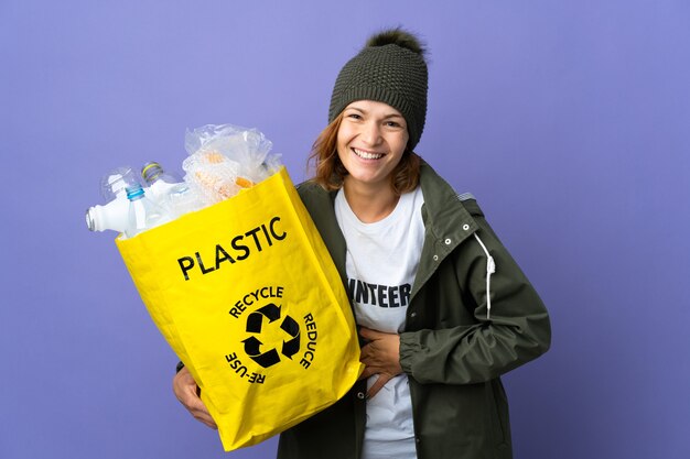 Junges georgianisches Mädchen, das eine Tasche voller Plastikflaschen hält, um viel lächelnd zu recyceln