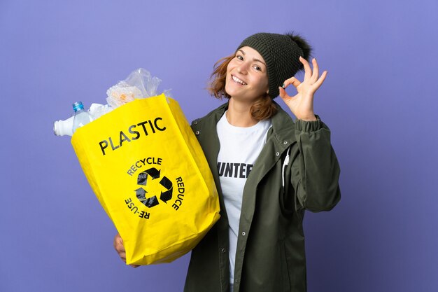 Junges georgianisches Mädchen, das eine Tasche voller Plastikflaschen hält, um zu zeigen, ok Zeichen mit den Fingern zeigend