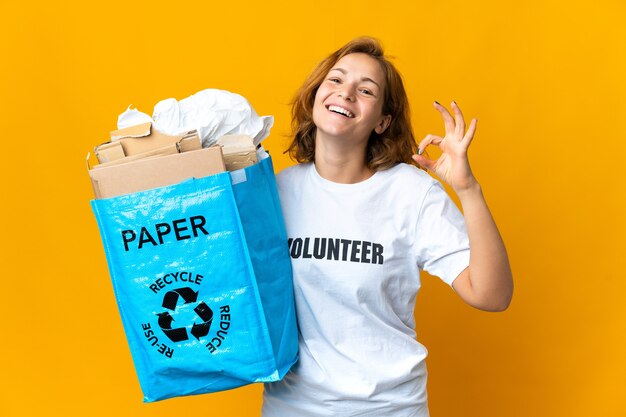 Junges georgianisches Mädchen, das einen Recyclingbeutel voll Papier hält, um das OK-Zeichen mit den Fingern zu recyceln