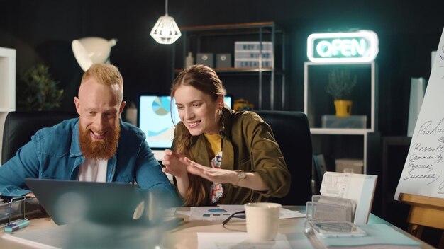 Foto junges geschäftspaar genießt projekt im nachtbüro. glückliches mädchen, das laptop tippt