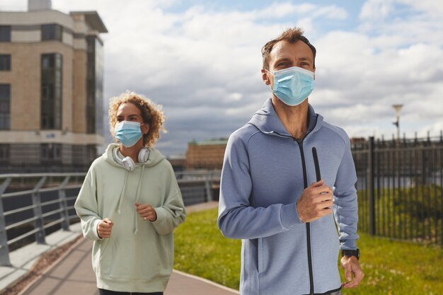 Foto junges gesundes paar in schutzmasken, die am morgen in der stadt zusammen joggen