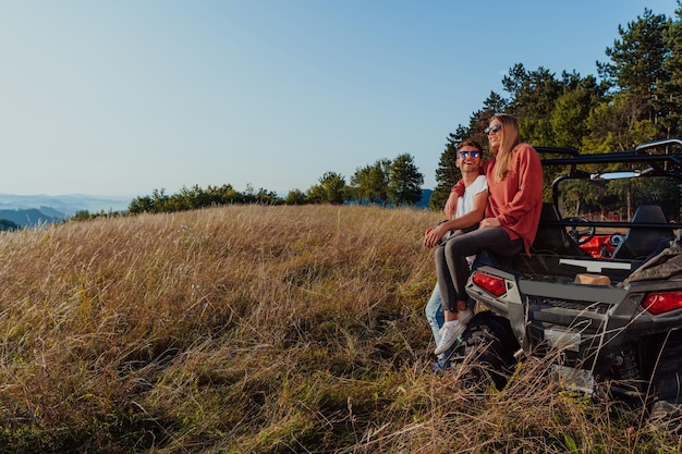 Junges glückliches aufgeregtes Paar, das einen schönen sonnigen Tag genießt, während es ein Off-Road-Buggy-Auto in der Bergnatur fährt.