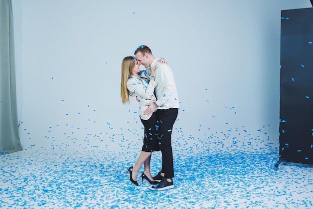 Junges glückliches Ehepaar, das sich in blauem Konfetti umarmt Ein verliebtes Paar freut sich und hat Spaß Gender-Fotosession
