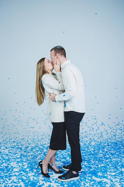 Junges glückliches Ehepaar, das sich in blauem Konfetti umarmt Ein verliebtes Paar freut sich und hat Spaß Gender-Fotosession