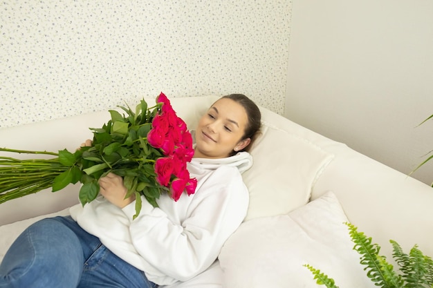 Junges glückliches Mädchen liegt mit einem Rosenstrauß auf dem Bett und sieht sie an