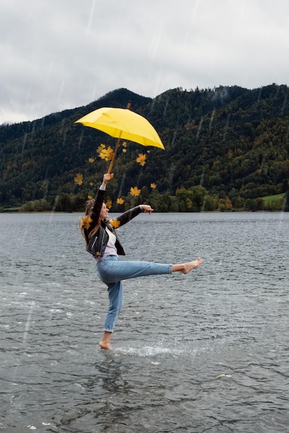 Junges glückliches Mädchen mit gelbem Regenschirm im Herbst im Regen