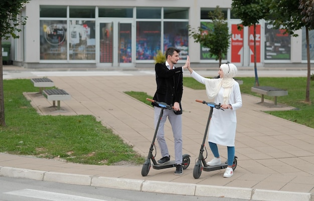 Junges glückliches muslimisches Paar, das Spaß daran hat, Elektroroller durch die Stadt zu fahren