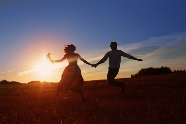 Junges glückliches paar, das auf sonnenuntergang springt