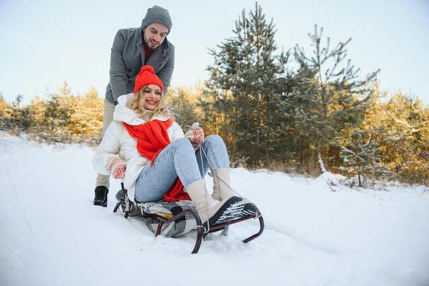 Junges glückliches Paar, das im Winter im Wald rodelt