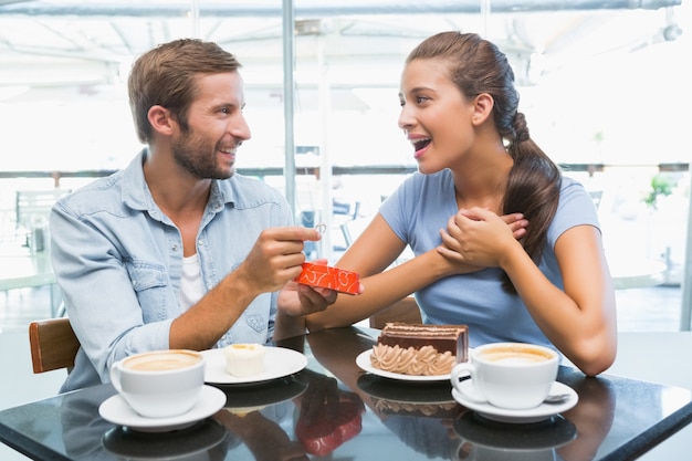 Junges glückliches Paar, das Kuchen essen und Mann, der ihr einen Ring gibt