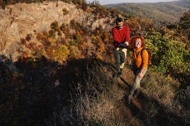 Junges glückliches Paar in der Liebe, die schönen sonnigen Herbsttag in der Natur verbringt. Paar, das Hände hält und den Hügel klettert.