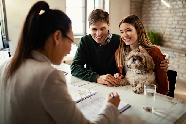 Junges glückliches Paar mit einem Hund bei einem Treffen mit einem Immobilienmakler im Büro