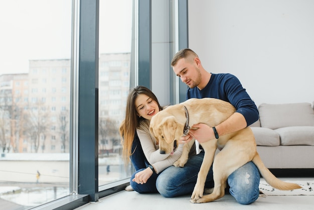 Junges glückliches Paar mit Hund, der zu Hause sitzt