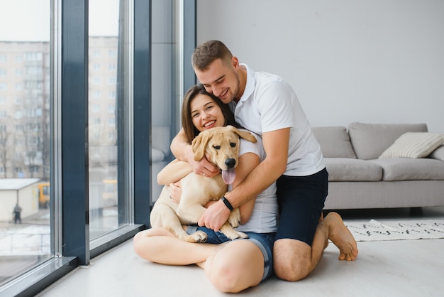 Junges glückliches Paar mit Hund, der zu Hause sitzt