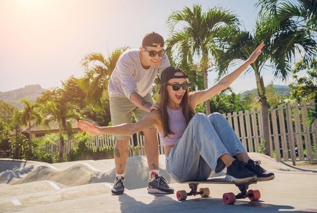 Junges glückliches Paar mit Skateboards genießt Longboarden im Skatepark