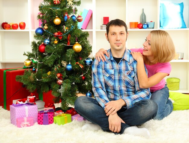 Junges glückliches Paar nahe einem Weihnachtsbaum zu Hause