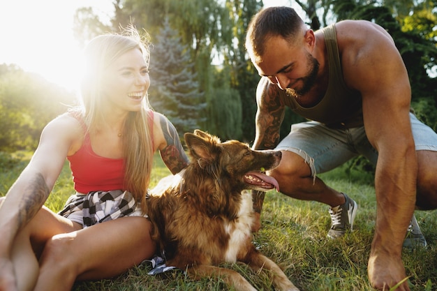 Junges glückliches Paar spielt mit ihrem Hund lächelnd im Park