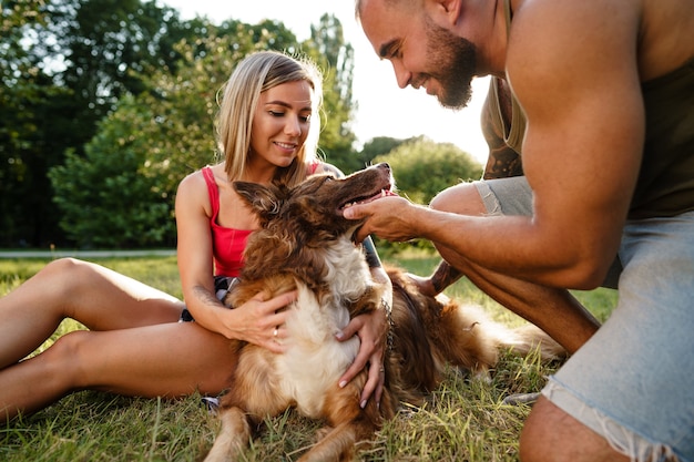 Junges glückliches Paar spielt mit ihrem Hund lächelnd im Park