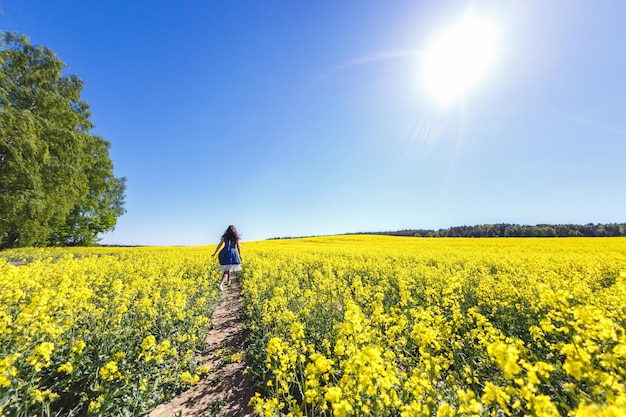 Junges, glückliches, schönes, großes Modellmädchen in blauem Kleid auf blühendem Rapsfeld im Sommer Folgen Sie mir Konzept