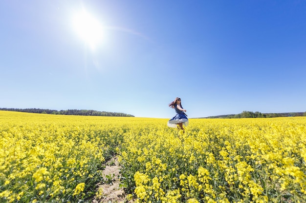 Junges, glückliches, schönes Mädchen in einem blauen Kleid auf blühendem Rapsfeld im Sommer Folgen Sie mir Konzept