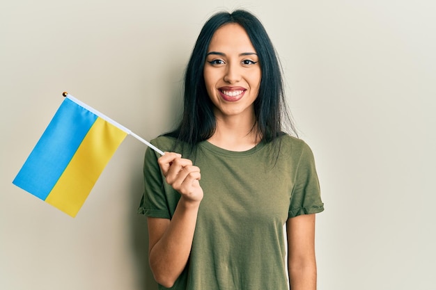 Junges hispanisches Mädchen mit ukraine-Flagge sieht positiv und glücklich aus und lächelt mit einem selbstbewussten Lächeln, das Zähne zeigt