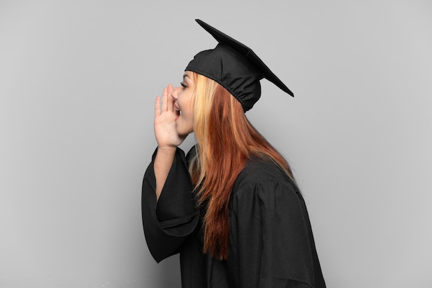 Junges Hochschulabsolventenmädchen über isoliertem Hintergrund schreien mit weit geöffnetem Mund zur Seite