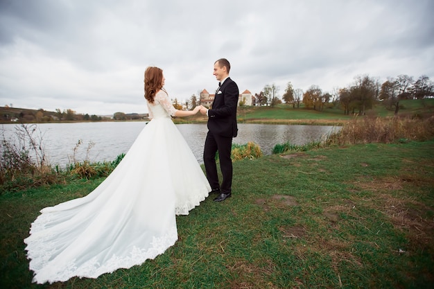 Junges Hochzeitspaar - frisch verheirateter Bräutigam und Braut, die an ihrem Hochzeitstag draußen posieren (farbiges Bild)