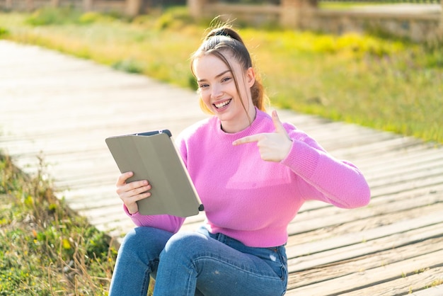 Junges hübsches Mädchen, das draußen eine Tablette hält und darauf zeigt