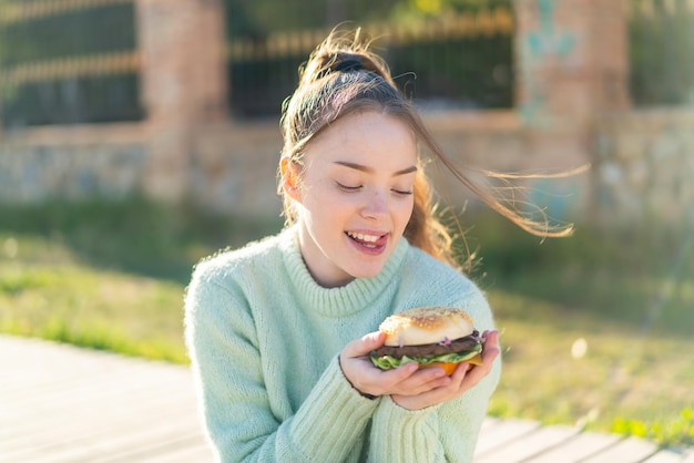 Junges hübsches Mädchen, das draußen einen Burger hält