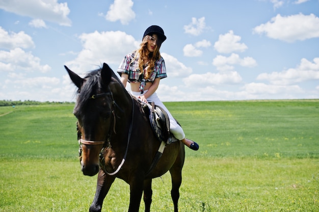 Junges hübsches Mädchen, das ein Pferd auf ein Feld am sonnigen Tag reitet.