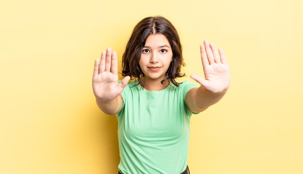 Junges hübsches Mädchen, das ernst, unglücklich, wütend und unzufrieden aussieht, das den Eintritt verbietet oder mit beiden offenen Handflächen aufhört