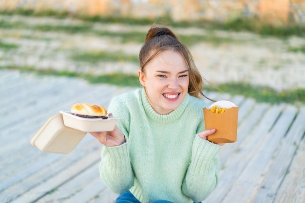 Junges hübsches Mädchen im Freien mit einem Burger und gebratenen Pommes