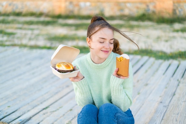 Junges hübsches Mädchen im Freien mit einem Burger und gebratenen Pommes