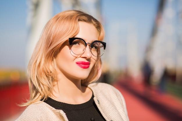 Junges hübsches Model trägt eine klare Brille mit hellem Make-up, die im Sonnenlicht posiert