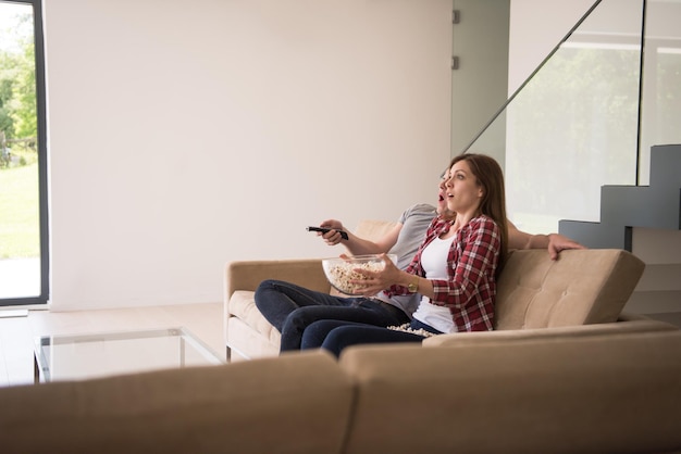 Foto junges hübsches paar, das seine freizeit beim fernsehen mit popcorn in seiner luxusvilla genießt